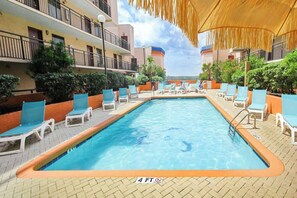 A rectangular swimming pool with a 4 FT depth marker, surrounded by lounge chairs and a covered area with a thatched roof. - Beach & Golf Vacation Dream (Myrtle Beach)