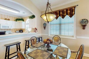 A dining area with a round glass table, wicker chairs, and a hanging light fixture. - Serene Barefoot Resort Condo (North Myrtle Beach)