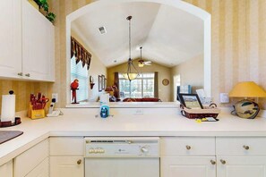 A kitchen with a built-in dishwasher, a large window, and a mirror reflecting the interior. - Serene Barefoot Resort Condo (North Myrtle Beach)