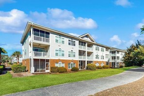 A multi-story residential building with balconies, a covered front porch, and a well-maintained lawn. - Serene Barefoot Resort Condo (North Myrtle Beach)