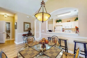 A dining area with a glass table, wicker chairs, and a hanging light fixture. - Serene Barefoot Resort Condo (North Myrtle Beach)