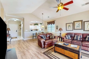 A spacious living room with a brown leather sofa, a coffee table, and a ceiling fan. - Serene Barefoot Resort Condo (North Myrtle Beach)
