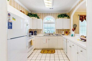 A kitchen with white cabinets, a central island, a window with blinds, and a tiled floor. - Serene Barefoot Resort Condo (North Myrtle Beach)