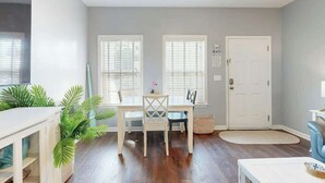 A room with a dining table, chairs, a white door, and a window with blinds. - Gulfstream Cottages 402 (Myrtle Beach)
