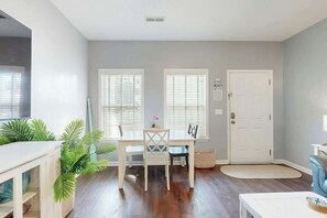 A room with a dining table, chairs, a white door, and a window with blinds. - Gulfstream Cottages 402 (Myrtle Beach)