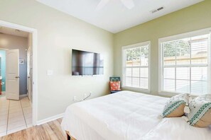 A bedroom with a bed, a television mounted on the wall, and a window with blinds. - Gulfstream Cottages 402 (Myrtle Beach)