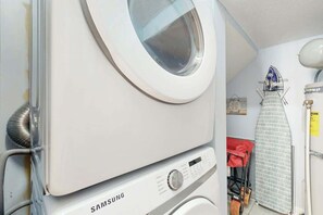 Eine Samsung Waschmaschine in einem Waschraum mit einem Wäscheständer und einem Bügelbrett.