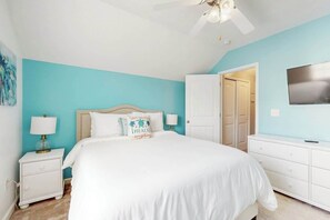 Ein Schlafzimmer mit einem Bett, Nachttischen, einem Schminktisch, einem Deckenventilator und einer Tür zu einem anderen Raum.