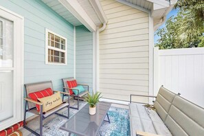 A covered outdoor seating area with two sofas and a table, a window, and a white fence. - Gulfstream Cottages 402 (Myrtle Beach)
