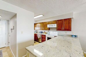A kitchen with wooden cabinets, a white microwave, and a granite countertop. - Sea Winds Unit 608 Condo (North Myrtle Beach)
