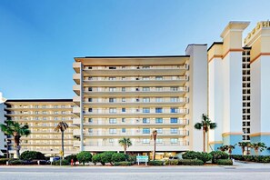 A multi-story hotel with a uniform facade, balconies on each floor, and a well-maintained landscaped area in front. - Sea Winds Unit 608 Condo (North Myrtle Beach)