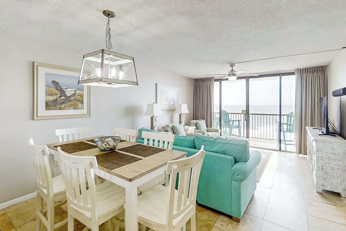 A dining area with a table and chairs, a teal sofa, and a balcony with a view.