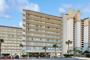 A multi-story hotel with a uniform facade, balconies, and a parking area with cars. - Sea Winds Unit 608 Condo (North Myrtle Beach)