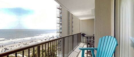 Uma varanda com vista para a praia e o oceano, uma cadeira azul e uma mesa.