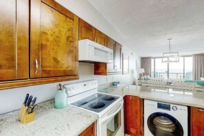 A compact kitchen with wooden cabinets, a microwave, a stove, and a washing machine. - Sea Winds Unit 608 Condo (North Myrtle Beach)