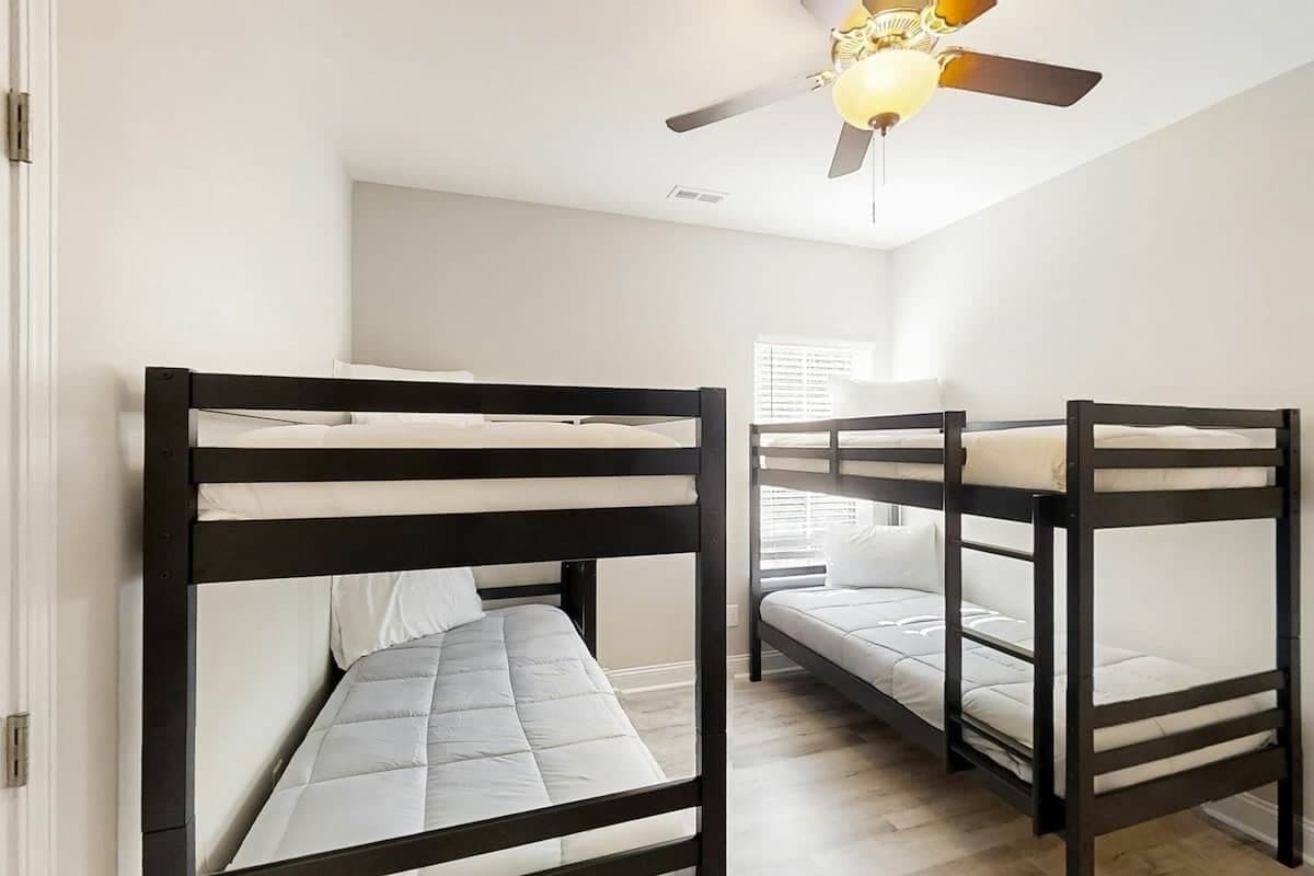 Ein Zimmer mit Etagenbetten, Deckenventilator und Fenster mit Jalousien.