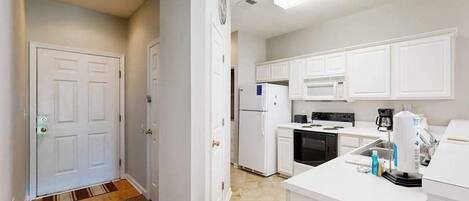 A kitchen with white cabinets, a refrigerator, a microwave, and a coffee maker.