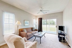 Ein Wohnzimmer mit Sofa, Sessel, Couchtisch, Fernseher und Deckenventilator.
