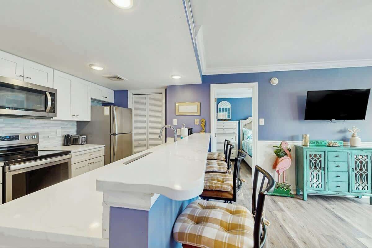 A modern kitchen with a central island, stainless steel appliances, and a teal-colored cabinet.