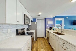 A kitchen with white cabinets, a microwave, a stove, and a sink. - Myrtle Shores Retreat (Myrtle Beach)