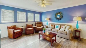 A living room with a blue wall, a ceiling fan, a sofa, two armchairs, a coffee table, and two lamps. - Myrtle Shores Retreat (Myrtle Beach)