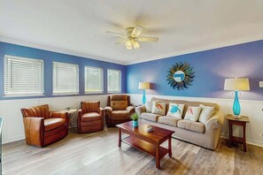 A living room with a blue wall, a ceiling fan, a sofa, two armchairs, a coffee table, and two lamps. - Myrtle Shores Retreat (Myrtle Beach)