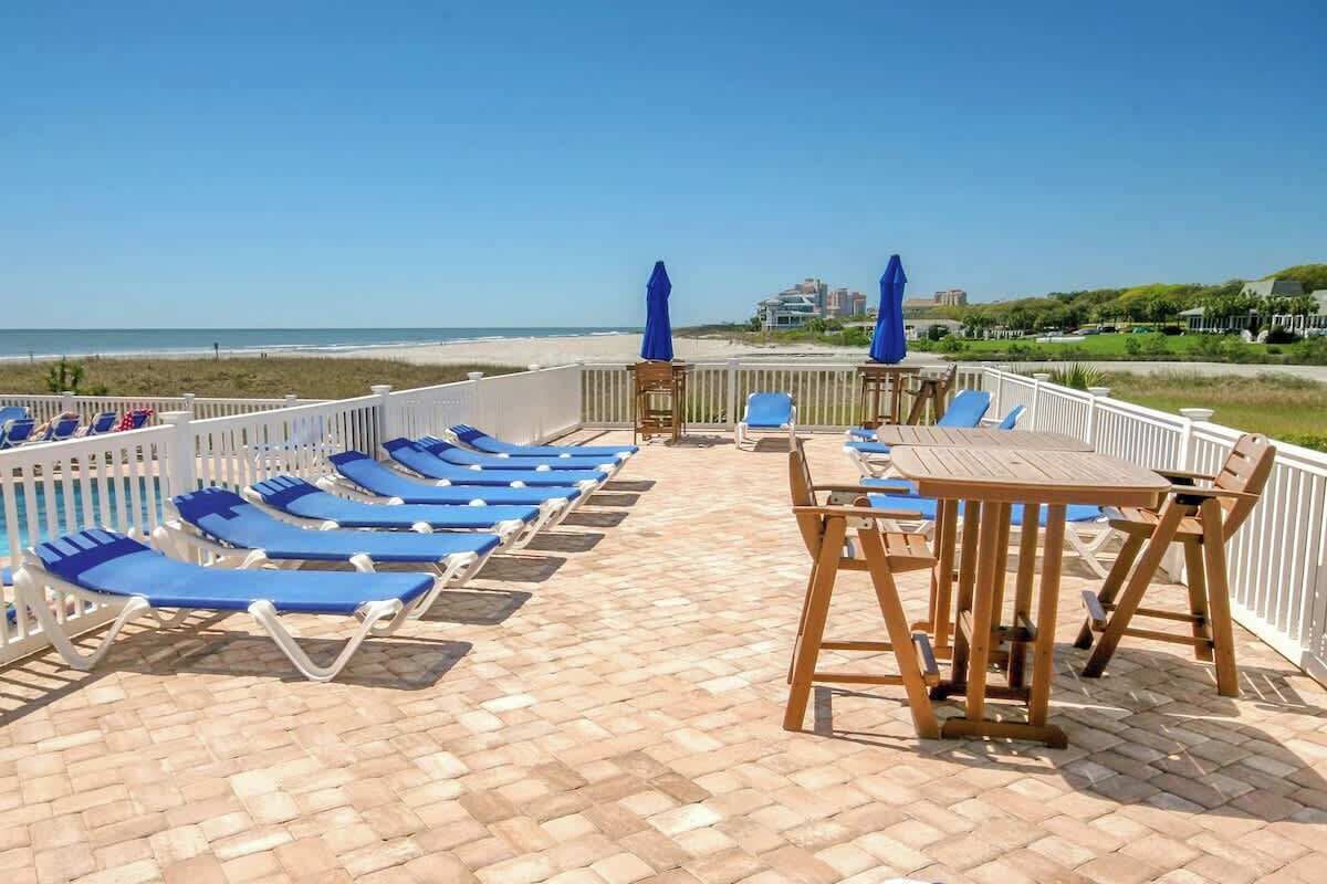 Een terras aan het strand met ligbedden en een tafel, met uitzicht op de oceaan.