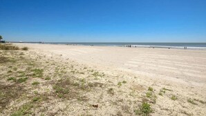 Een strand met een heldere lucht, een zandstrand en enkele mensen in de verte.