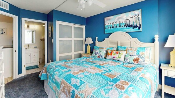 Een slaapkamer met een bed, een plafondventilator, een schilderij en een deur naar een andere kamer.
