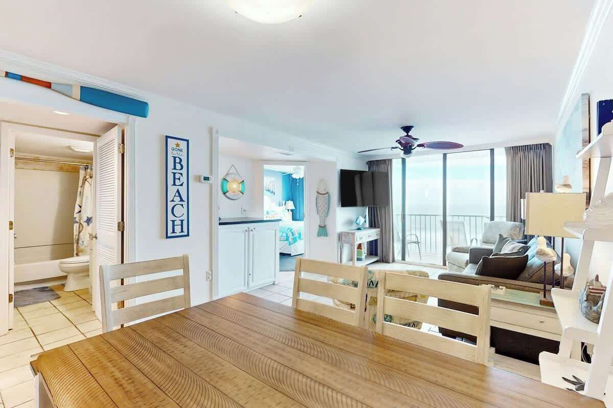 Amplia sala de estar con una mesa de comedor de madera, sillas blancas, un sofá y un balcón con vistas.