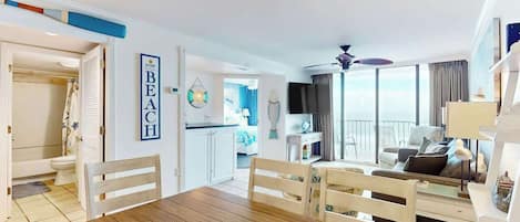 Amplia sala de estar con una mesa de comedor de madera, sillas blancas, un sofá y un balcón con vistas.