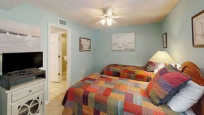 A bedroom with two beds, a ceiling fan, a television on a stand, and artwork on the walls. - Little Big House at Windy Hill (North Myrtle Beach)