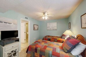 A bedroom with two beds, a ceiling fan, a television on a stand, and artwork on the walls. - Little Big House at Windy Hill (North Myrtle Beach)