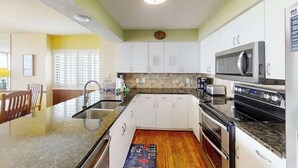 A modern kitchen with white cabinets, a granite countertop, a built-in microwave, and a stove. - Little Big House at Windy Hill (North Myrtle Beach)
