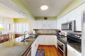 A modern kitchen with white cabinets, a granite countertop, a built-in microwave, and a stove. - Little Big House at Windy Hill (North Myrtle Beach)