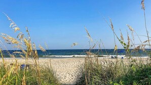 A beach with a clear sky, waves, and tall grasses in the foreground. - Little Big House at Windy Hill (North Myrtle Beach)