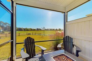 Un balcon avec deux fauteuils Adirondack, une table et une vue sur un champ verdoyant.