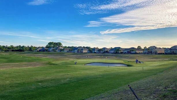 Camp de golf amb prat d'herba, búnquer de sorra i una bassa.