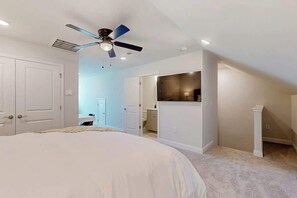 Ein Schlafzimmer mit einem Bett, einem Deckenventilator und einem durch eine offene Tür einsehbaren Badezimmer.