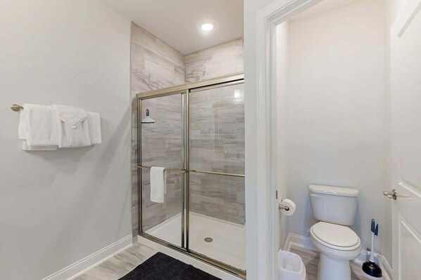 Une salle de bain moderne avec une douche à parois de verre, des toilettes et un tapis noir.