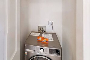 Eine kompakte, frontbeladene Waschmaschine aus Edelstahl mit Bedienfeld, einer Steckdose und einem kleinen Ablagebereich für Tide Waschmittelkartuschen.
