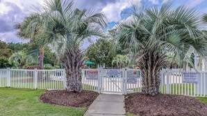 A gated entrance with palm trees and a pathway leading to a private property. - River Oaks Unit 61M Condo (Myrtle Beach)