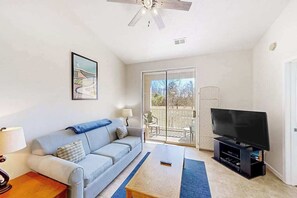 A living room with a sofa, coffee table, TV, and a balcony with a view. - Golfside Escape | River Oaks Sixty-One M (Myrtle Beach)