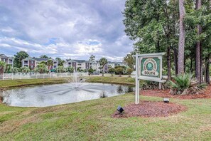 A sign indicating a golf course and tennis resort with a pond and residential buildings in the background. - Golfside Escape | River Oaks Sixty-One M (Myrtle Beach)