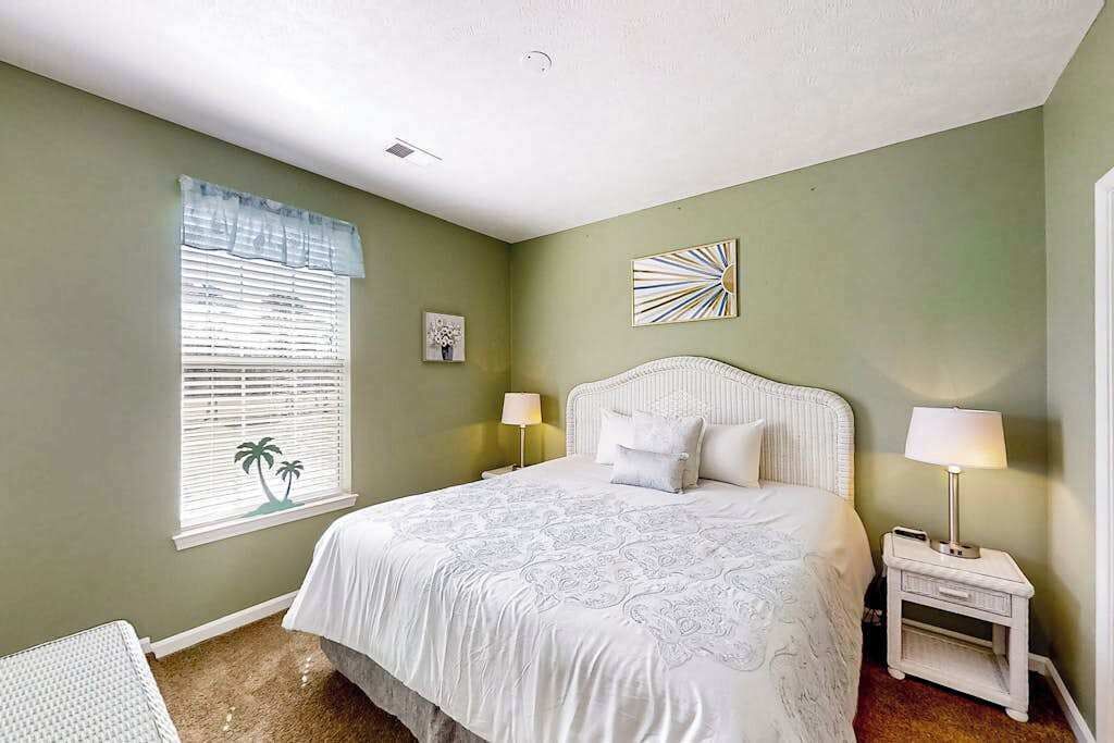 Un dormitorio con cama, lámparas de noche, una ventana con persianas y un cuadro en la pared.