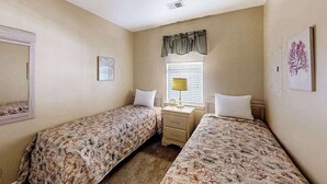 A bedroom with two single beds, a bedside table with a lamp, a window with blinds, and a wall-mounted mirror. - River Oaks Unit 61M Condo (Myrtle Beach)