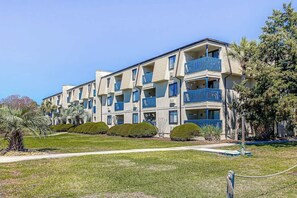 Un immeuble résidentiel à plusieurs étages, doté de balcons, d’une pelouse bien entretenue et surplombant un ciel dégagé.
