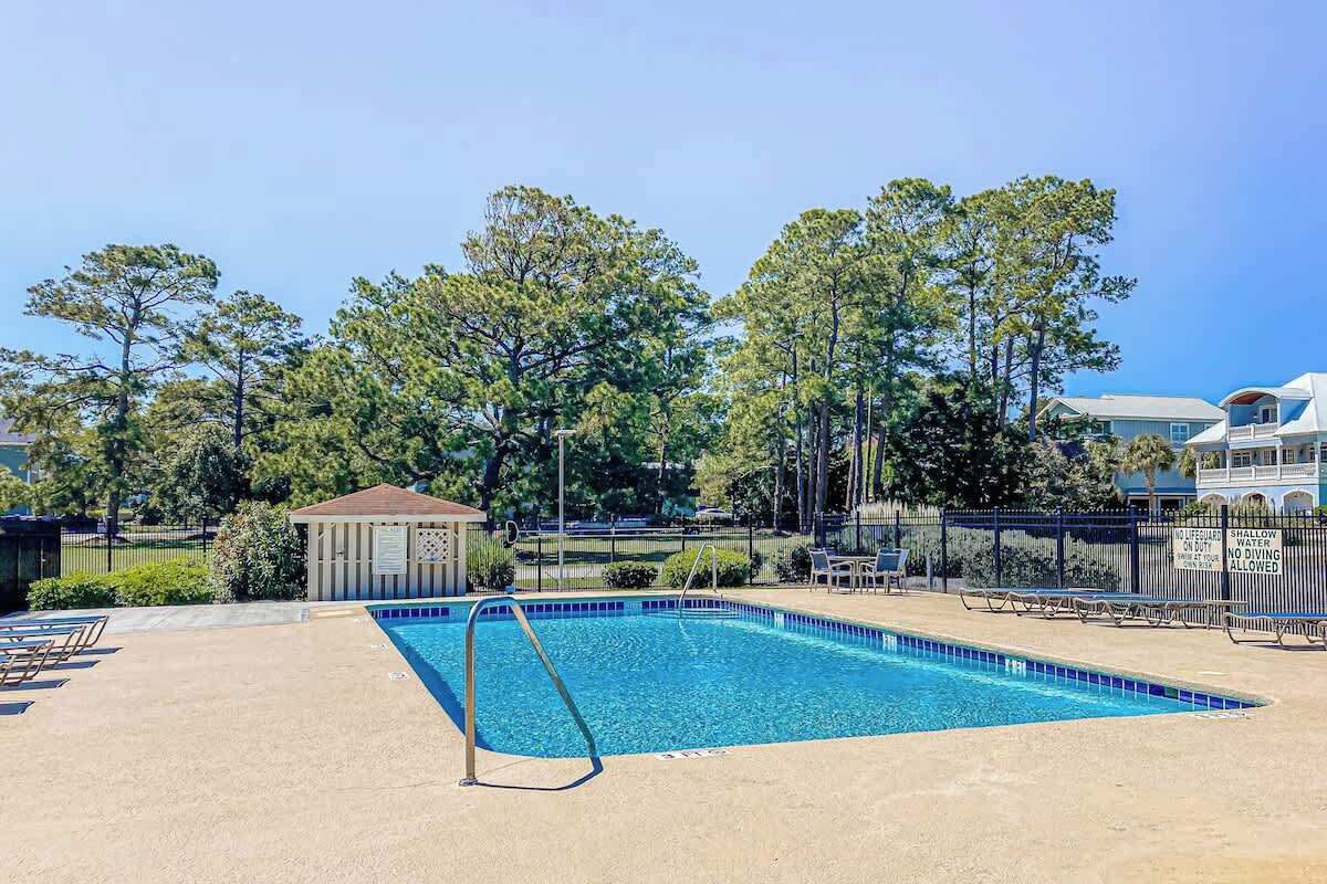 A swimming pool with a small pavilion, lounge chairs, and a fence with a warning sign.