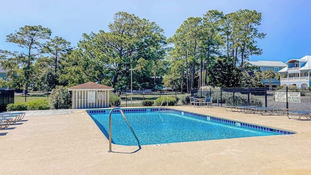 A swimming pool with a small pavilion, lounge chairs, and a fence with a warning sign. - Beach Happy Place Retreat (North Myrtle Beach)