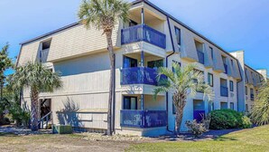 A multi-story residential building with balconies, palm trees, and a clear sky. - Beach Happy Place Retreat (North Myrtle Beach)